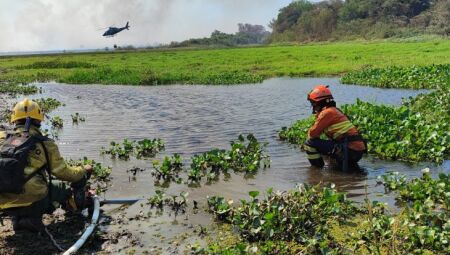 Bombeiros observam helicóptero de apoio pelo ar enquanto recolhem água para abastecer o trabalho de combate ao fogo no Pantanal