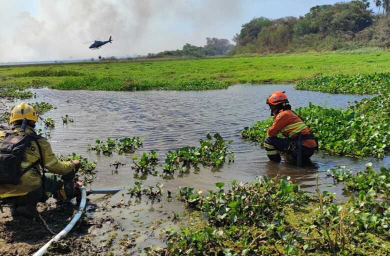 Bombeiros observam helicóptero de apoio pelo ar enquanto recolhem água para abastecer o trabalho de combate ao fogo no Pantanal