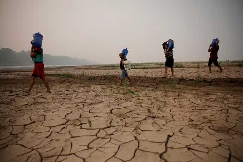 Ribeirinhos carregam galões de água enquanto atravessam bancos de areia