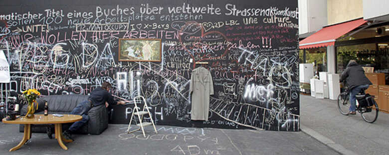 Homem escreve com giz na obra "Muro da Paz", instalada na capital alemã; obra faz parte da Bienal de Arte de Berlim