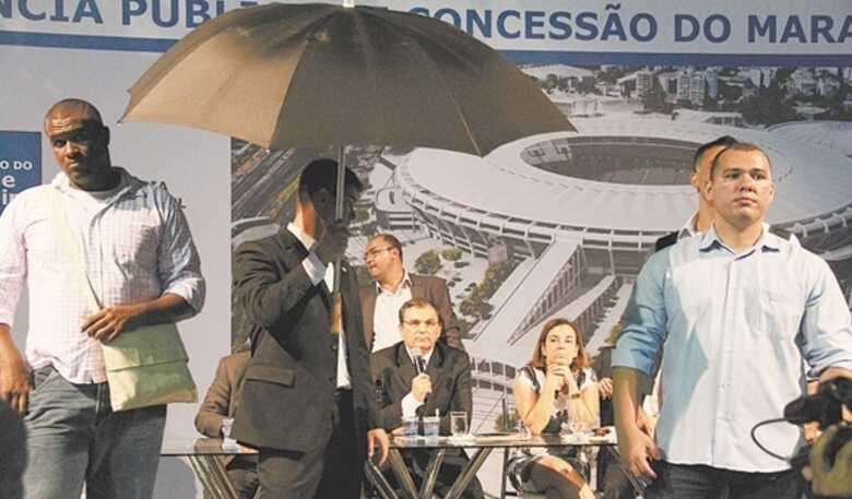 Segurança usa guarda-chuva para proteger as autoridades da chuva de ovo, papel e casca de banana.