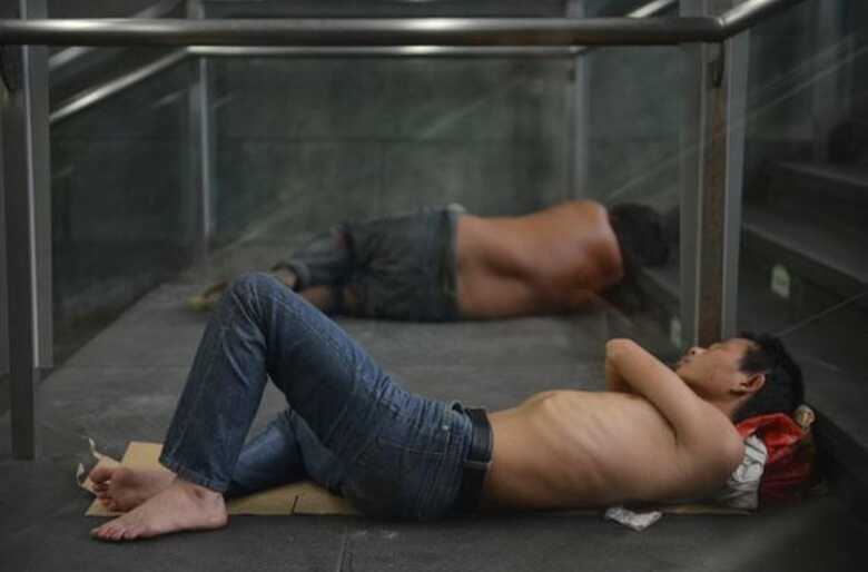 Moradores tentam se abrigar do calor em entrada de estação de metrô nesta quarta-feira (31) em Xangai. (Foto: Peter Parks/AFP)