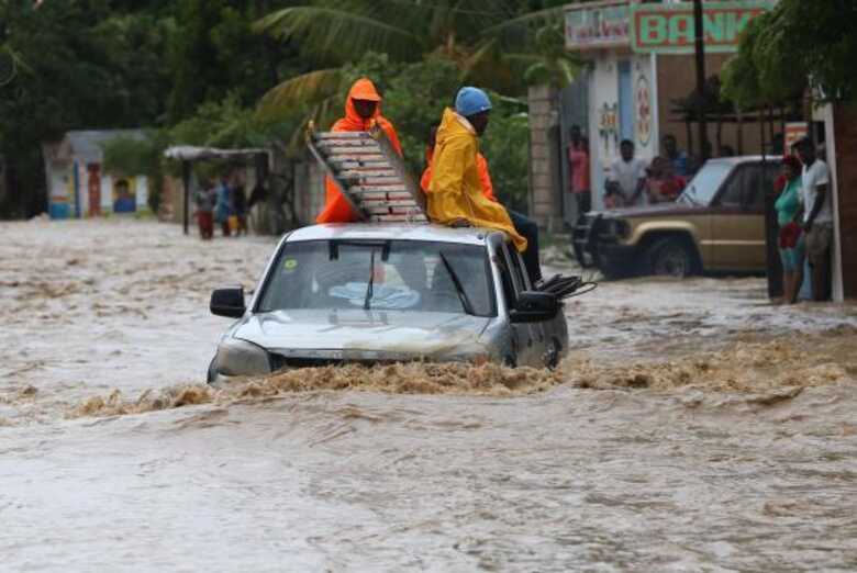 Um grupo de pessoas tenta cruzar uma via alagada em Leogane, no Haiti, após a passagem do Furacão Matthew.