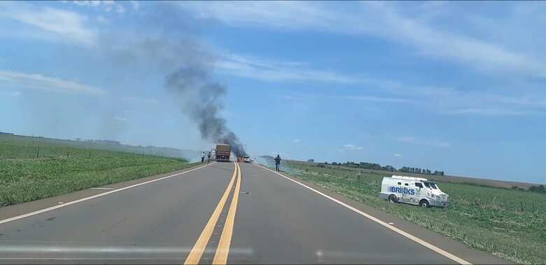 Carro-forte e atrás a fumaça do veículo usado no assalto, incendiado pelos bandidos