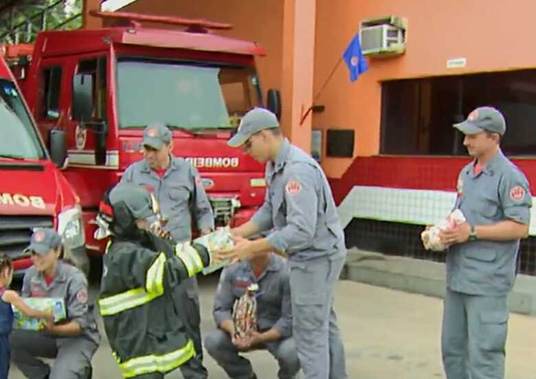 Kauê vestido de bombeiro recebendo presentes da corporação